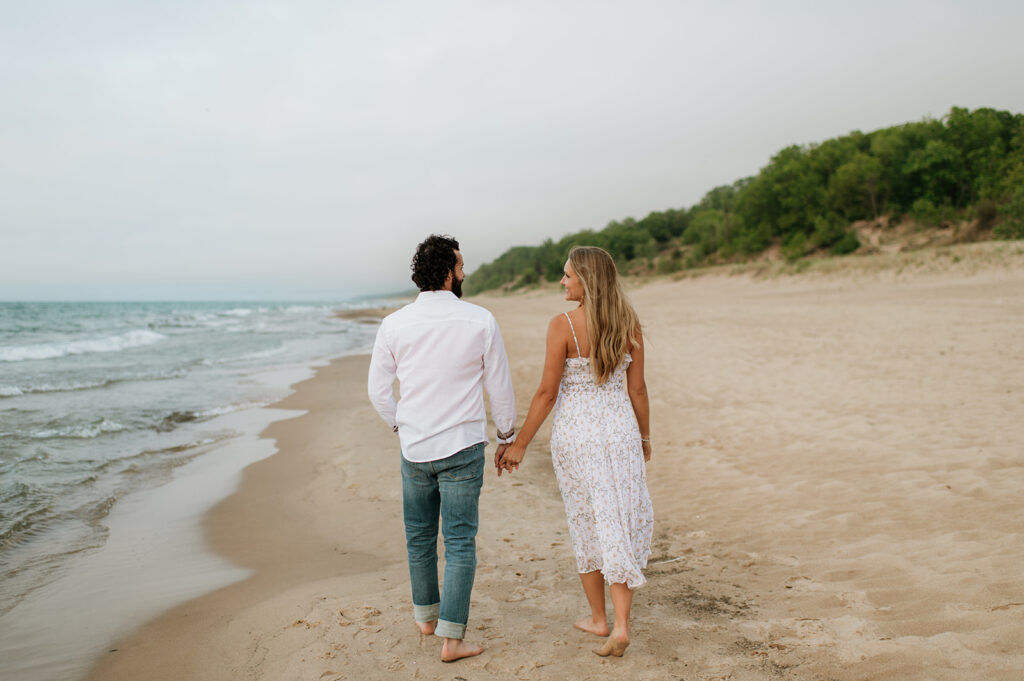 Couple walking along the shoreline at Indiana Dunes National Park for their beach engagement photos