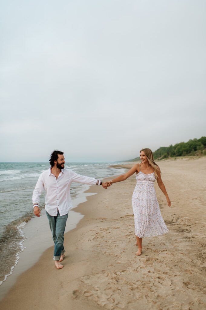 Couple walking along the shoreline at Indiana Dunes National Park for their beach engagement photos
