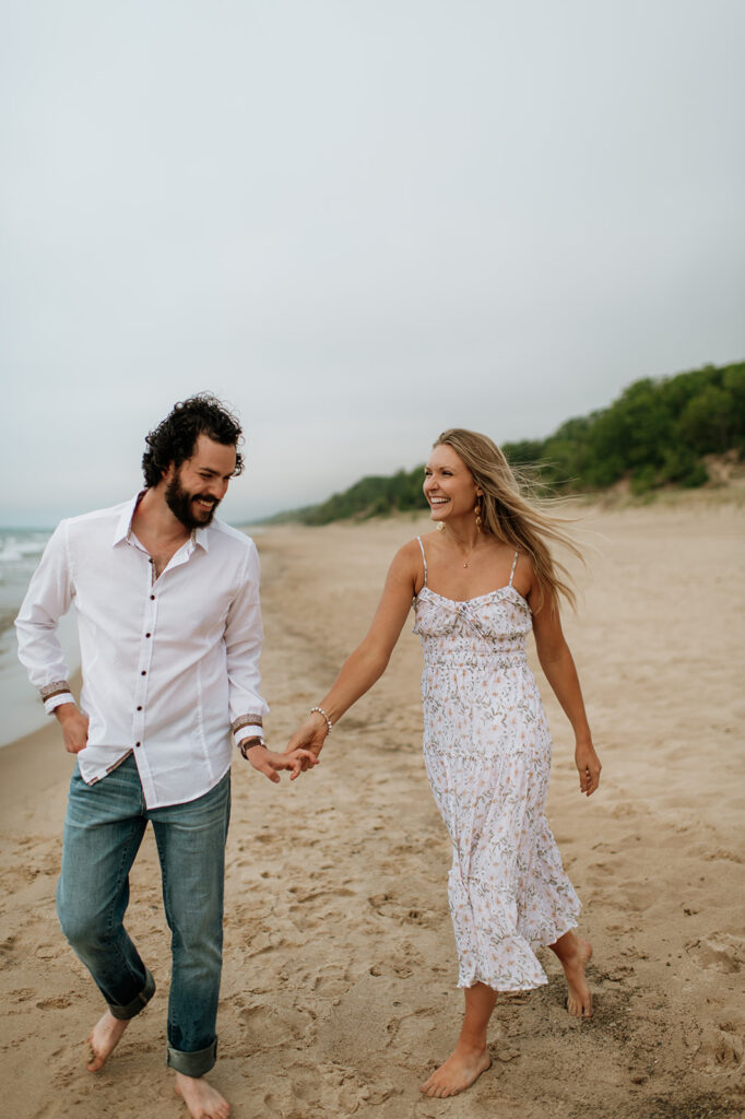 Couple walking along the shoreline at Indiana Dunes National Park for their beach engagement photos