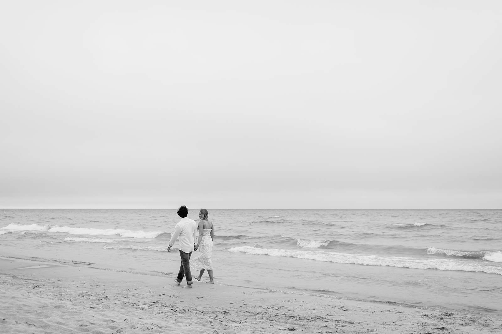 Couple walking along the shoreline at Indiana Dunes National Park for their beach engagement photos