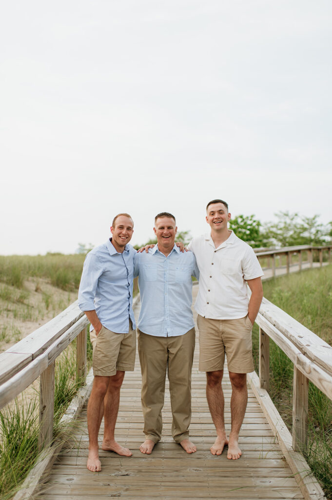 Three men posing together on a boardwalk during their extended family photoshoot at New Buffalo Beach in Michigan
