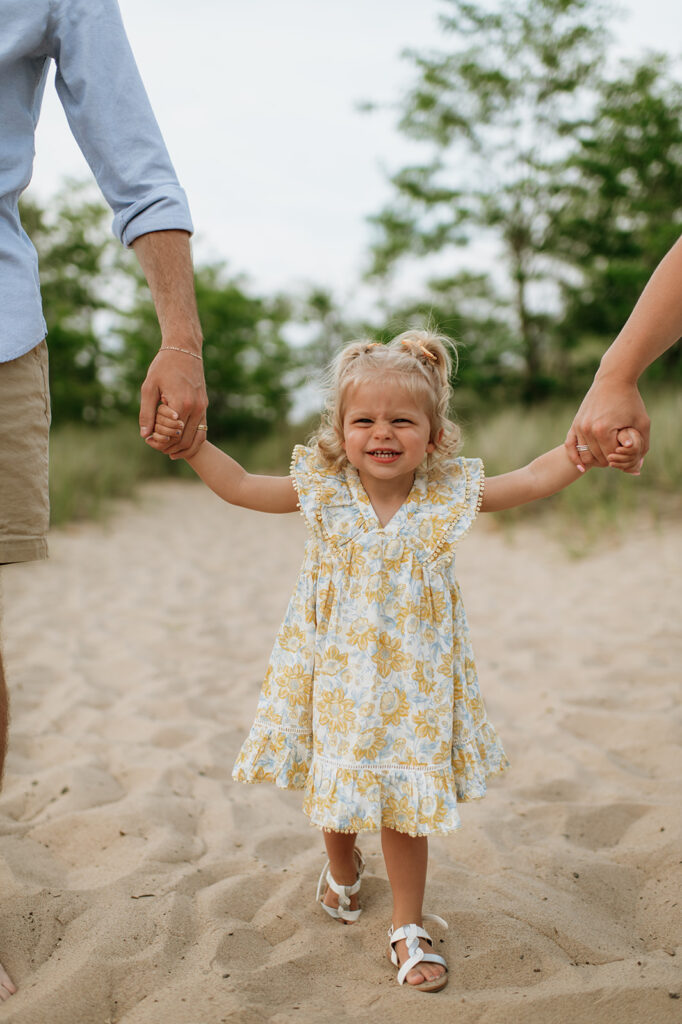 Little girl holding hands with her parents on the beach