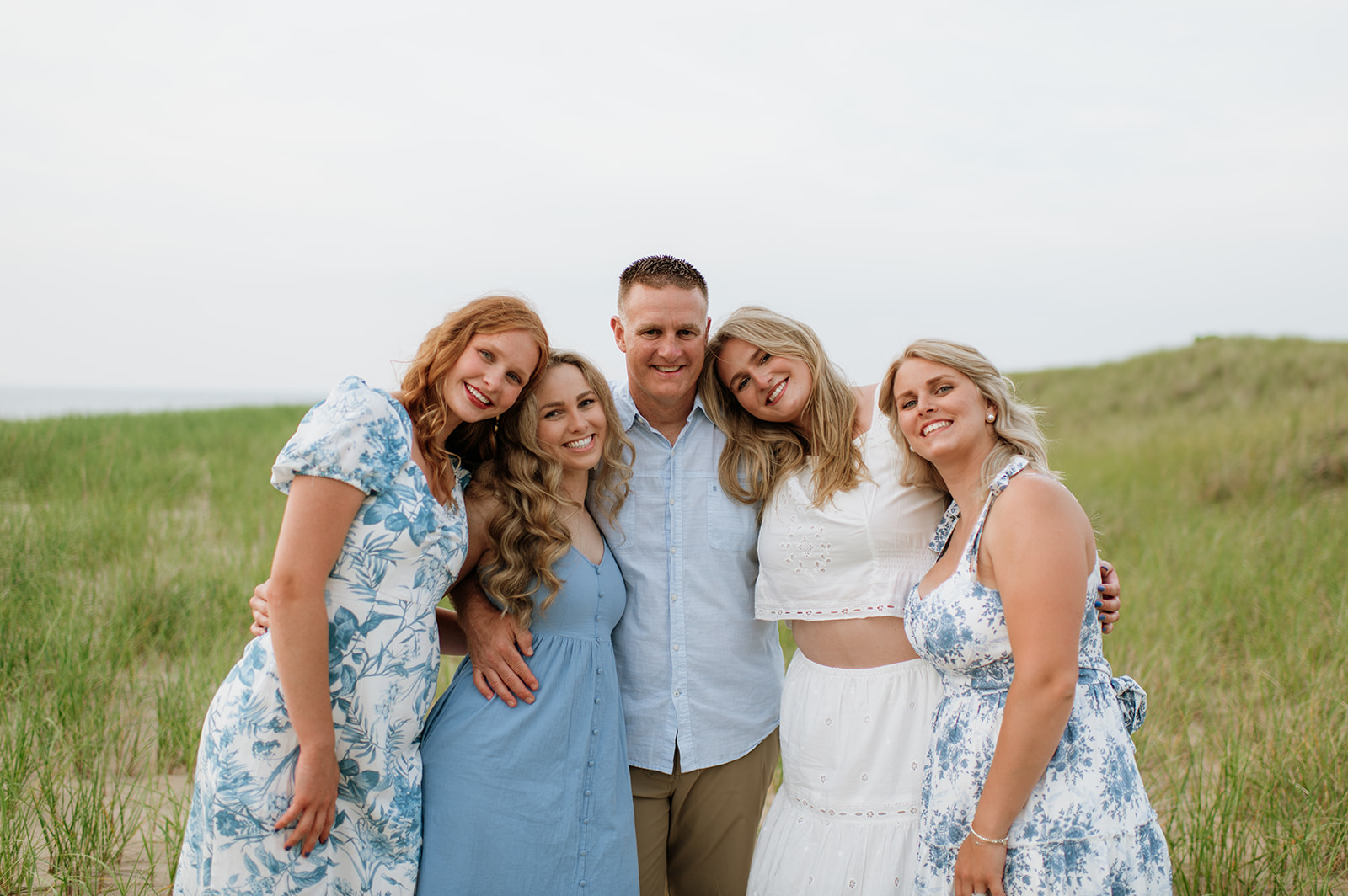 Father posing with his four grown daughter during their extended family photoshoot in New Buffalo, Michigan