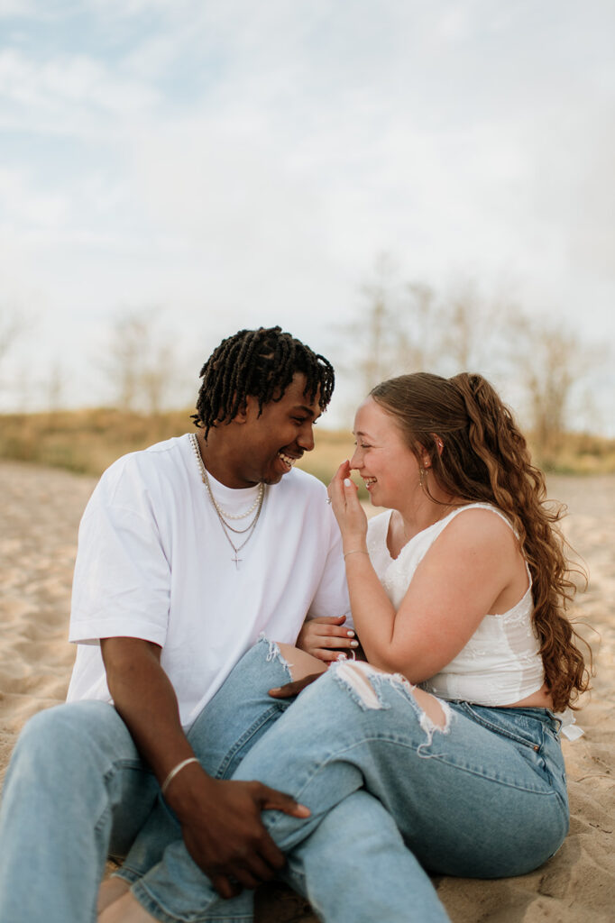 Couple laughing while sitting in the sand on New Buffalo beach in Southwest Michigan