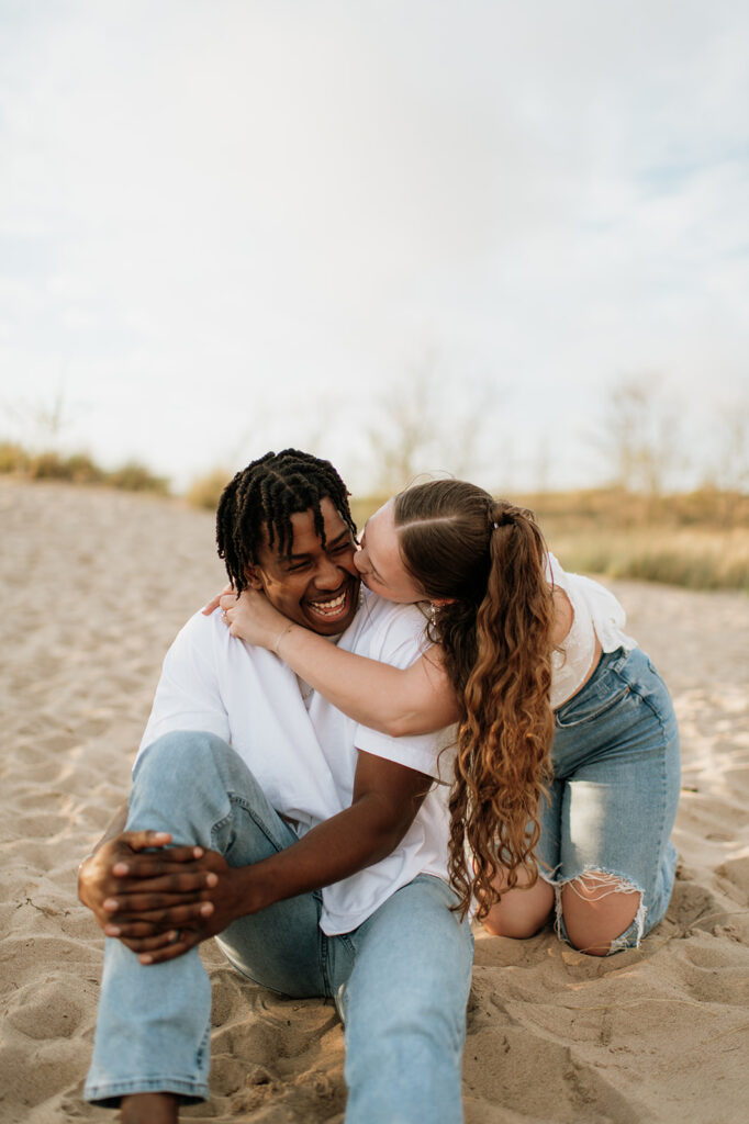Woman kissing her fiancé during their beach engagement session in Michigan