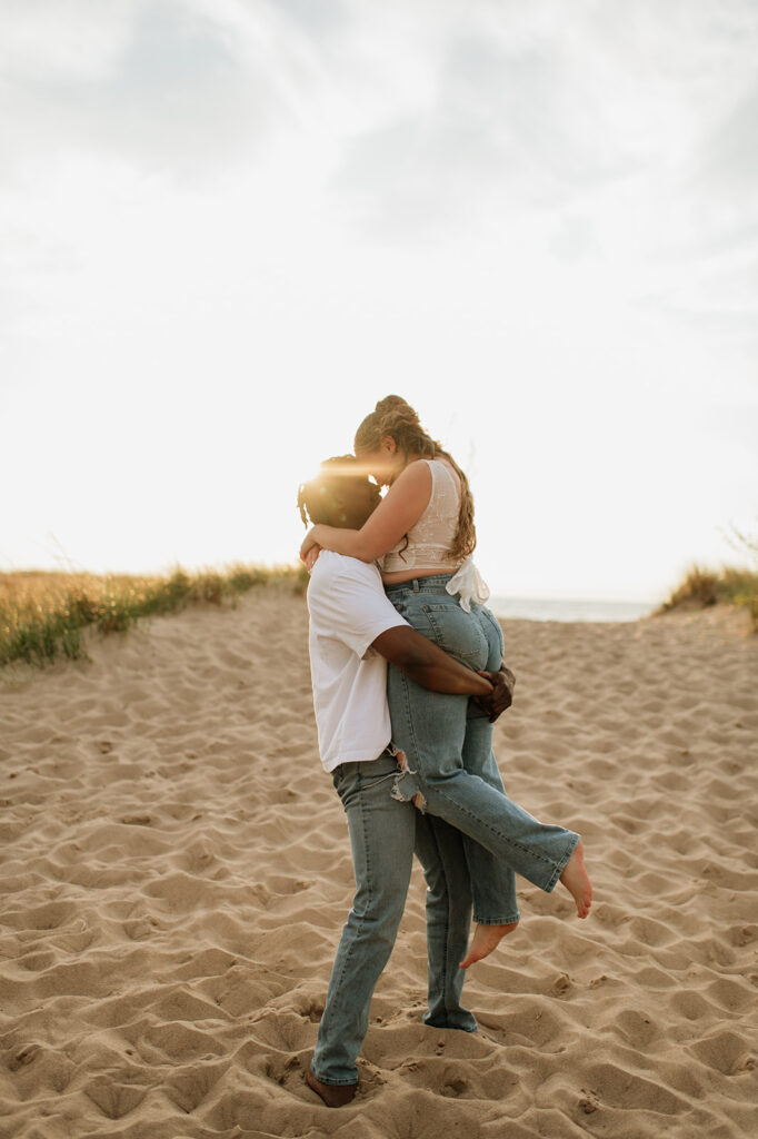Man picking up his fiancé during their New Buffalo beach engagement photos in Southwest, Michigan