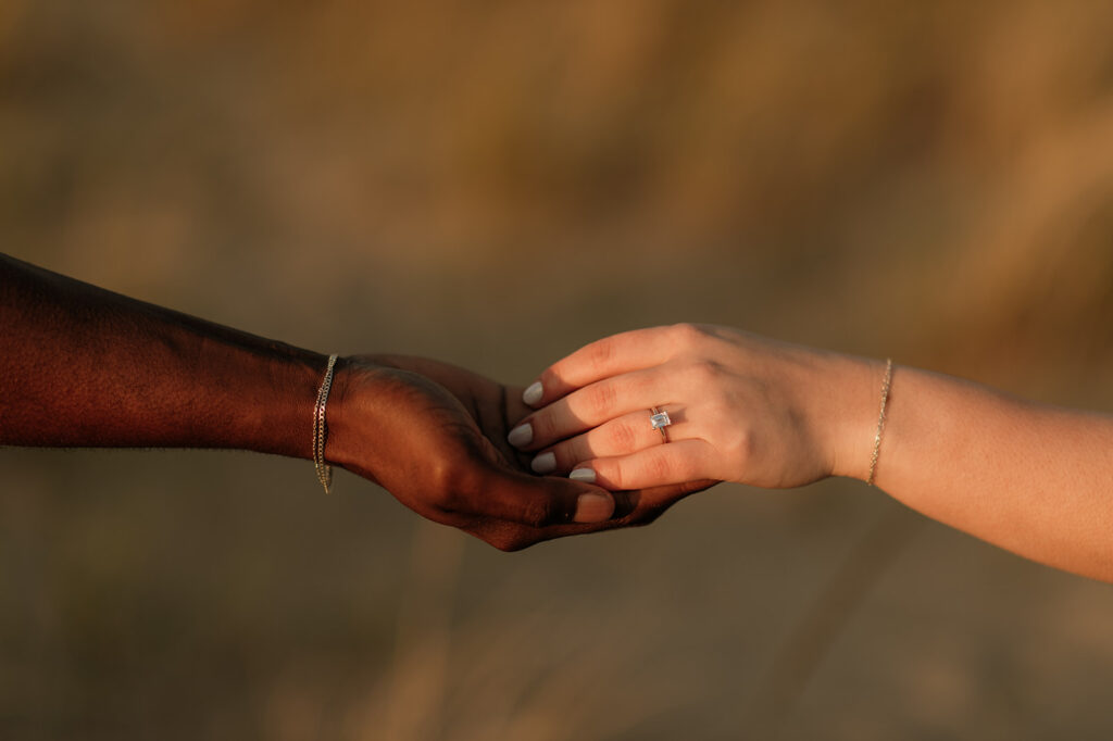Engagement photo detail shot of a couple touching hands on the beach