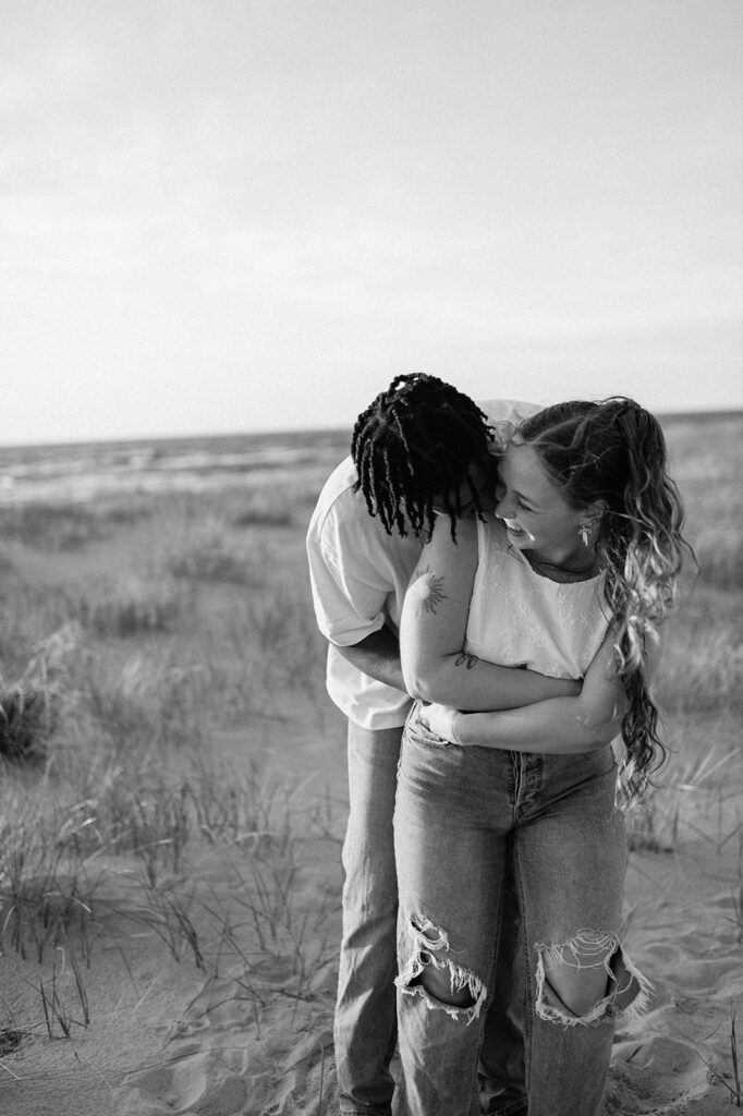 Black and white photo of a couple being playful during their beach engagement shoot