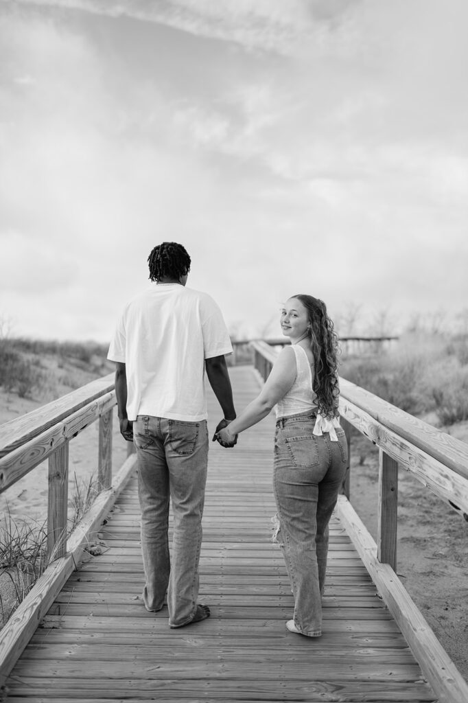 Black and white photo of a couple walking on the boardwalk for their Southwest Michigan engagement photos at New Buffalo Beach