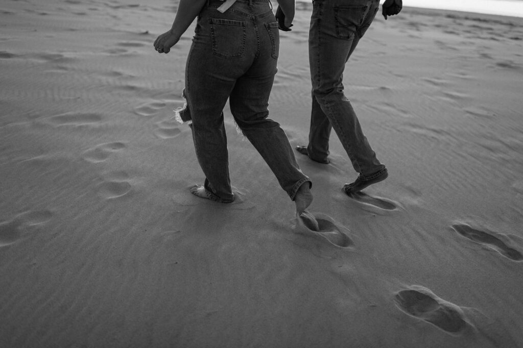Close up black and white photo of a couple running along the beach and leaving footprints in the sand