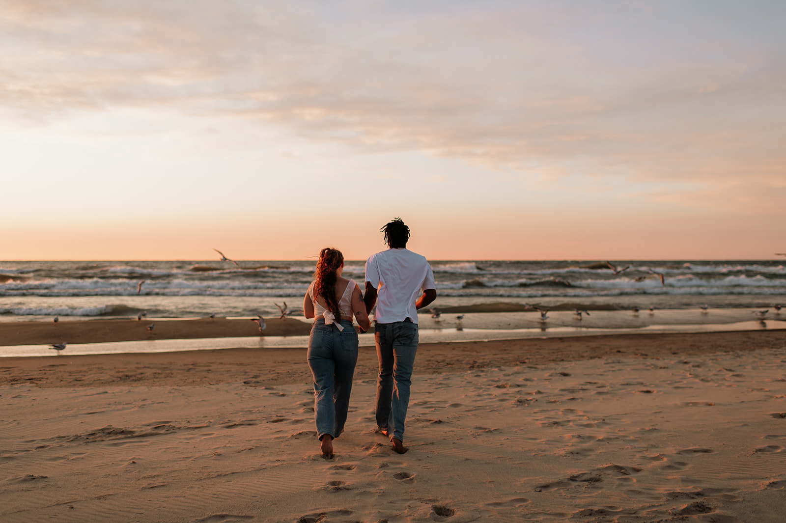 Couple running towards Lake Michigan during their engagement session at New Buffalo beach