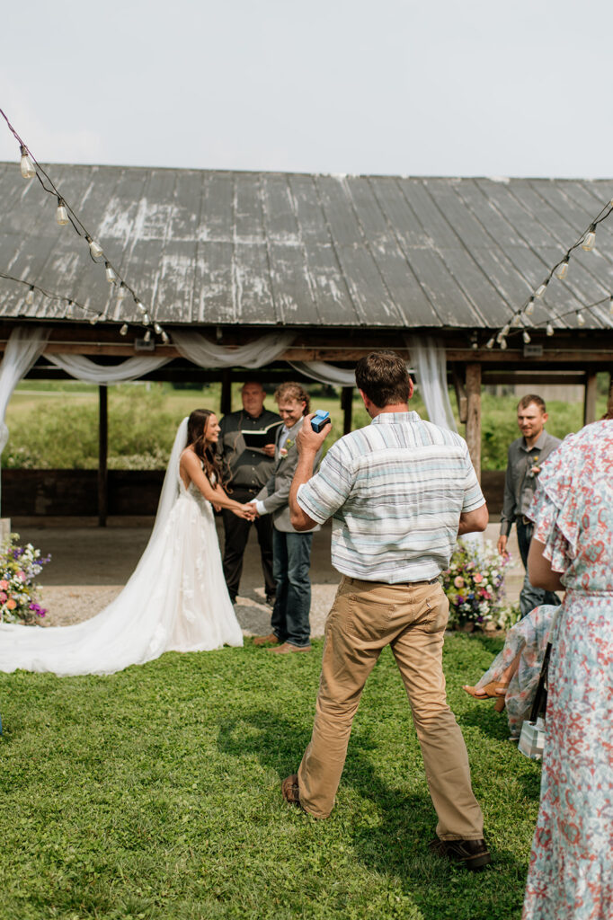 Wedding guest bringing up the rings to the bride and groom