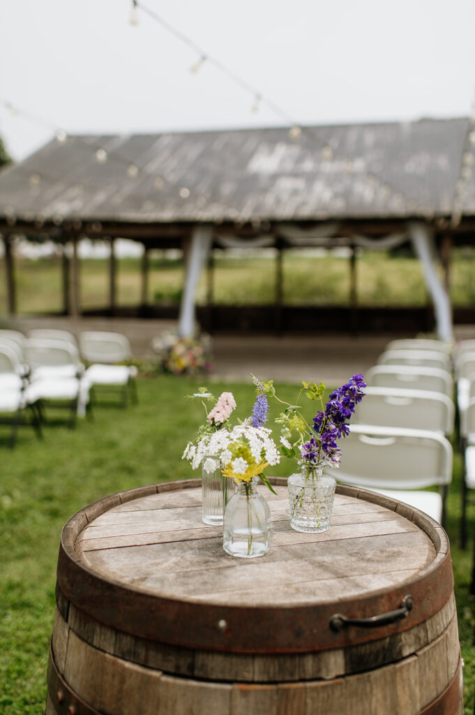 Close-up of a wooden barrel topped with mason jars of colorful wildflowers at 5C Farms ceremony setup.