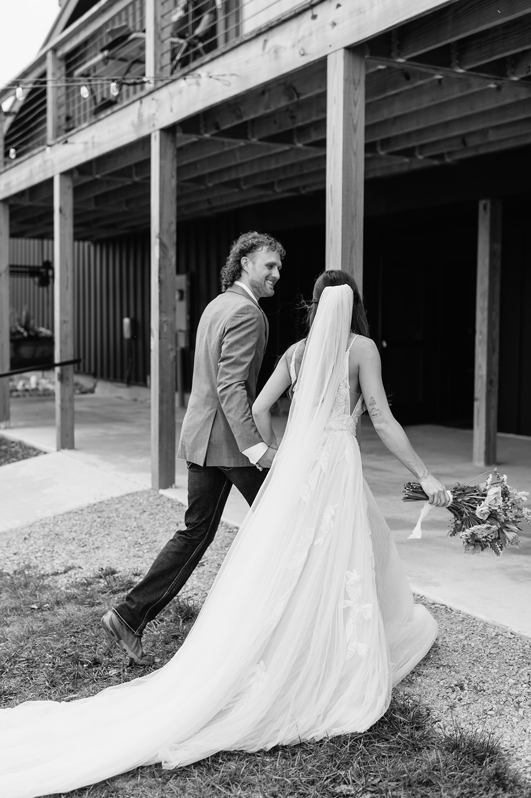 Black and white photo of the bride and groom walking back into 5C Farms wedding venue after their ceremony