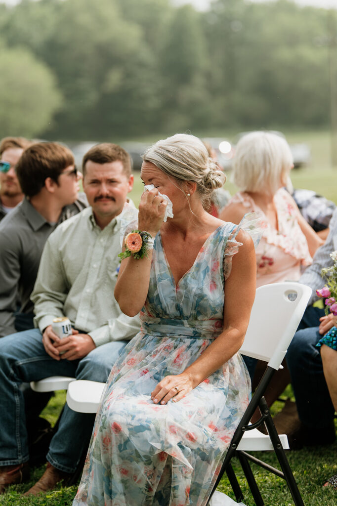 Emotional mother of the bride in a floral dress wiping away tears during the ceremony at 5C Farms.