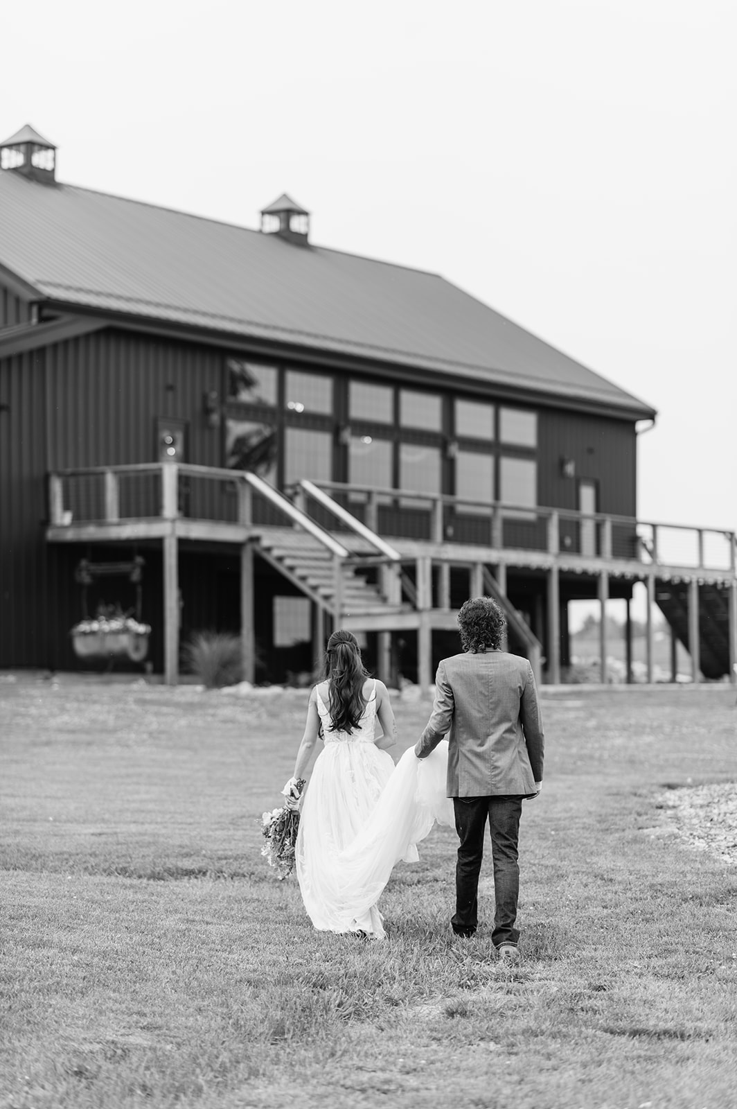 Black and white photo of a bride and groom walking to 5c Farms wedding venue - Premier Indiana barn wedding venue