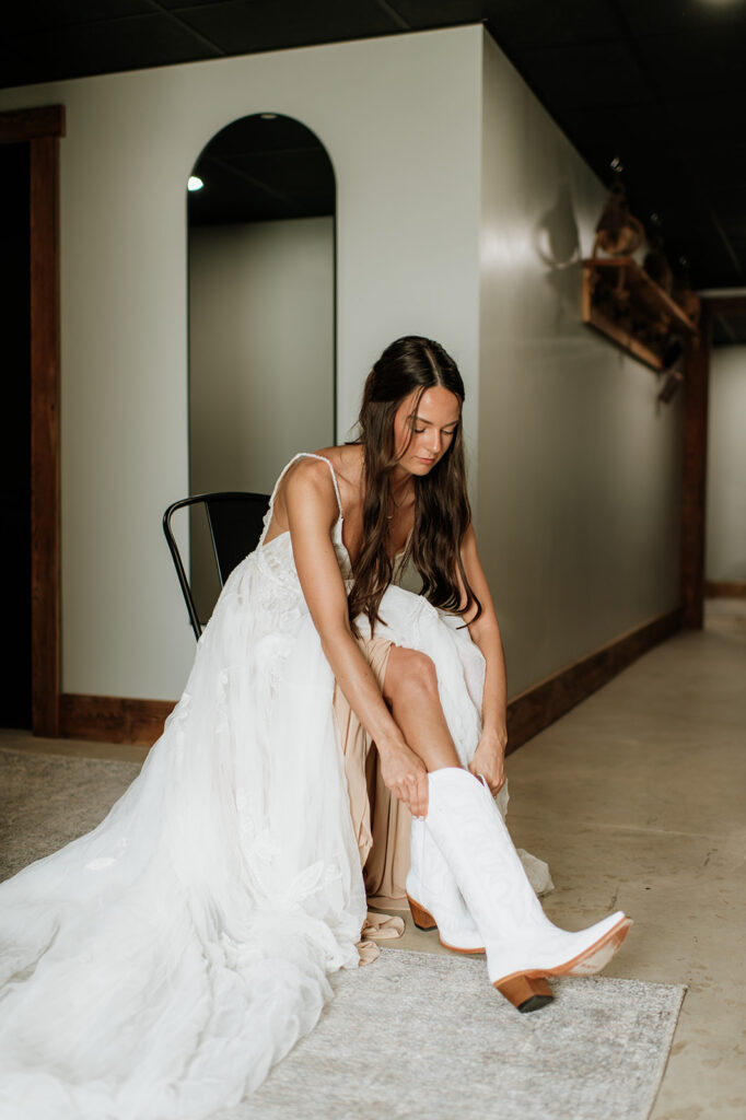 Bride putting on her white cowgirl boots for her 5c Farms wedding in Albion, Indiana
