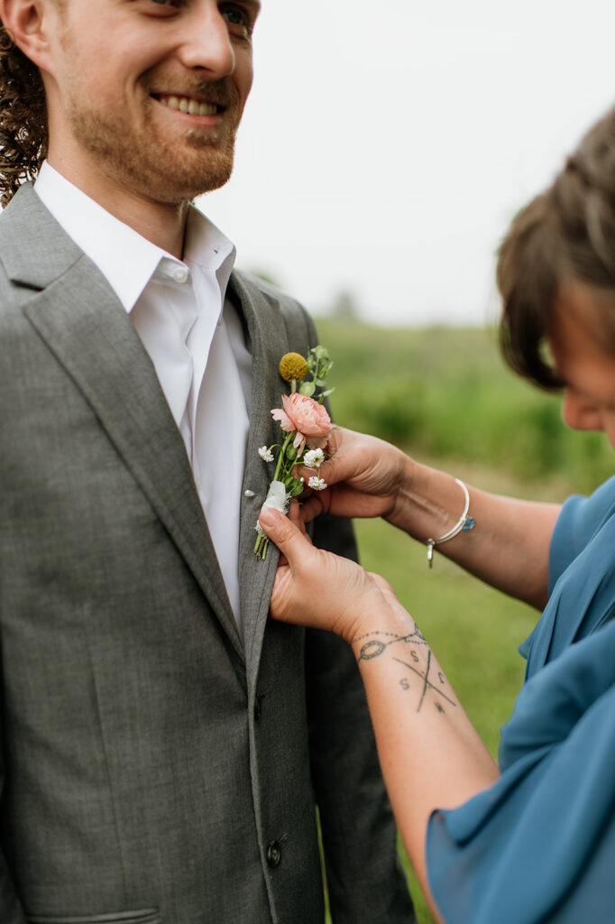 Grooms mother putting on his boutonniere for him