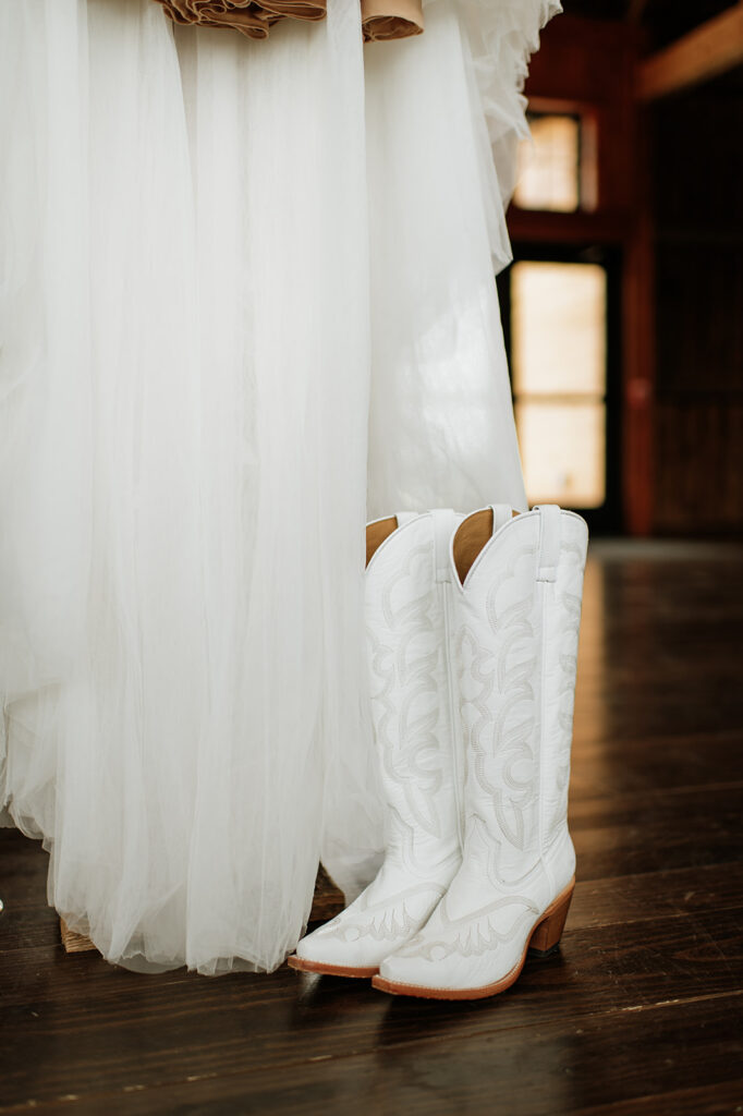 Close up shot of brides white cowgirl boots next to her dress