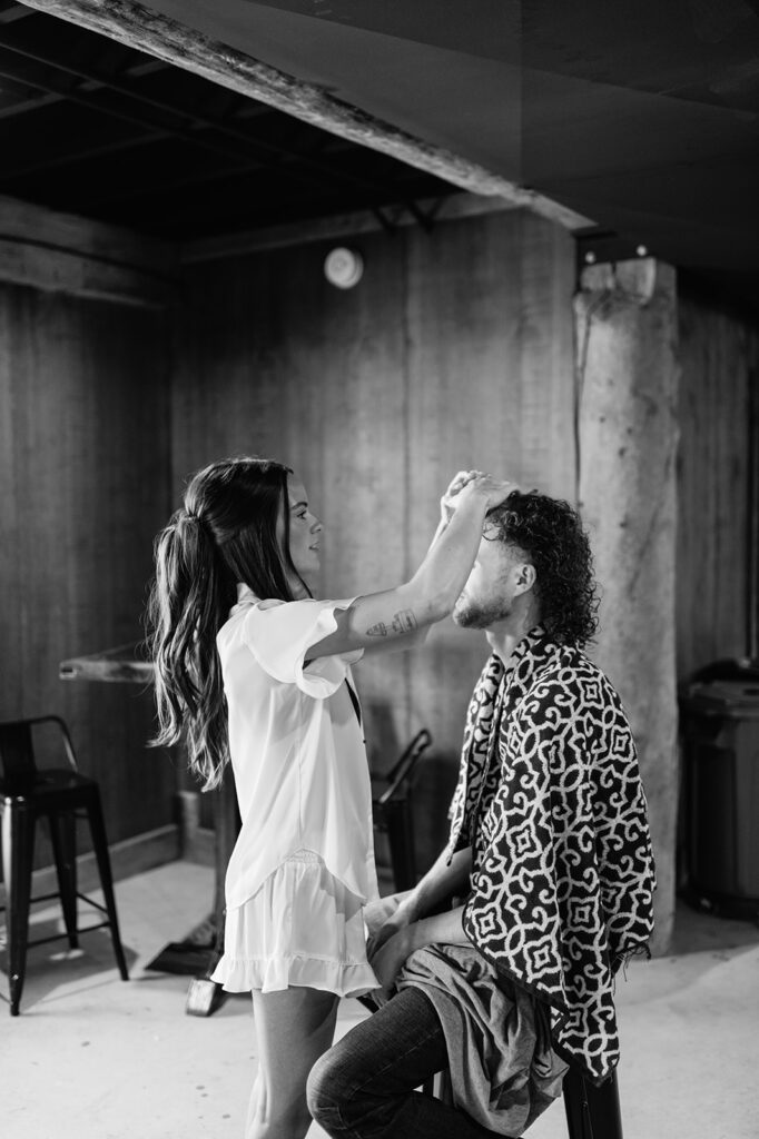 Black and white photo of the bride doing the grooms hair for their wedding
