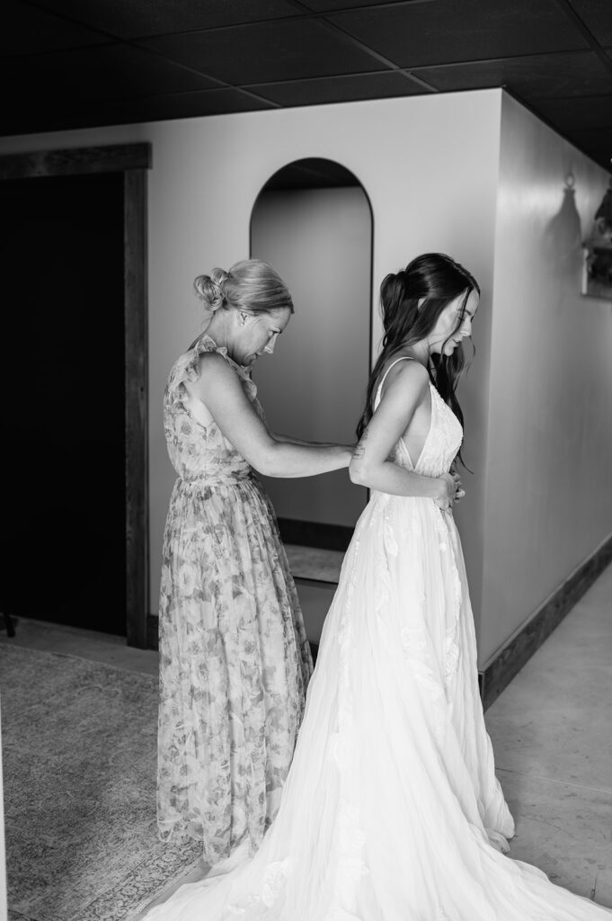 Black and white photo of a brides mother helping her into her wedding dress