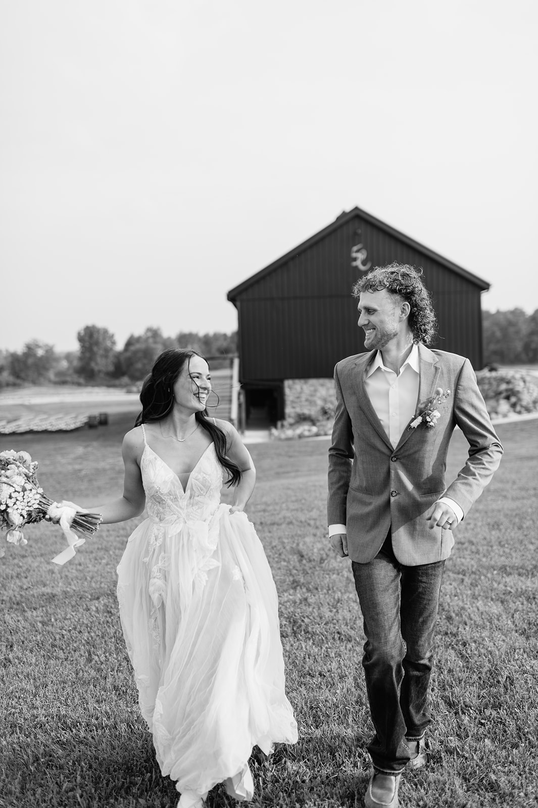 Black-and-white photo of bride and groom running outside 5C Farms with the barn in the background.
