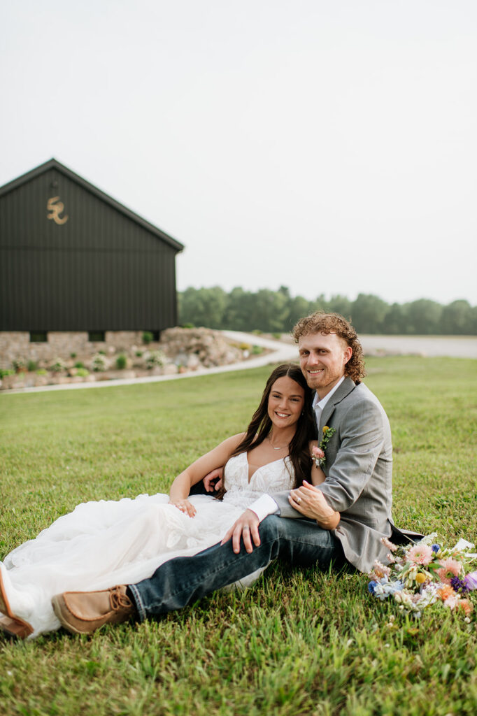 Bride and groom sitting in the grass outside of 5C Farms - Premier Indiana barn wedding venue