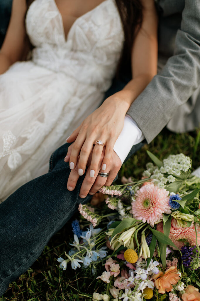 Close up shot of a bride and groom with their hands overlapping and the brides colorful bouquet 