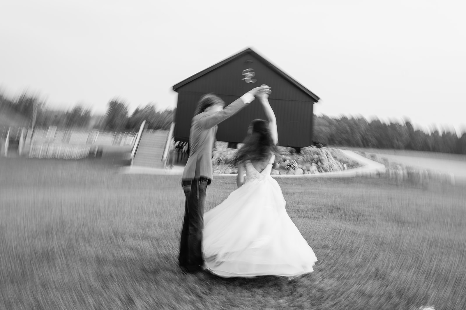Black-and-white photo of groom twirling bride on the lawn in front of the barn at 5C Farms - Premier Indiana barn wedding venue