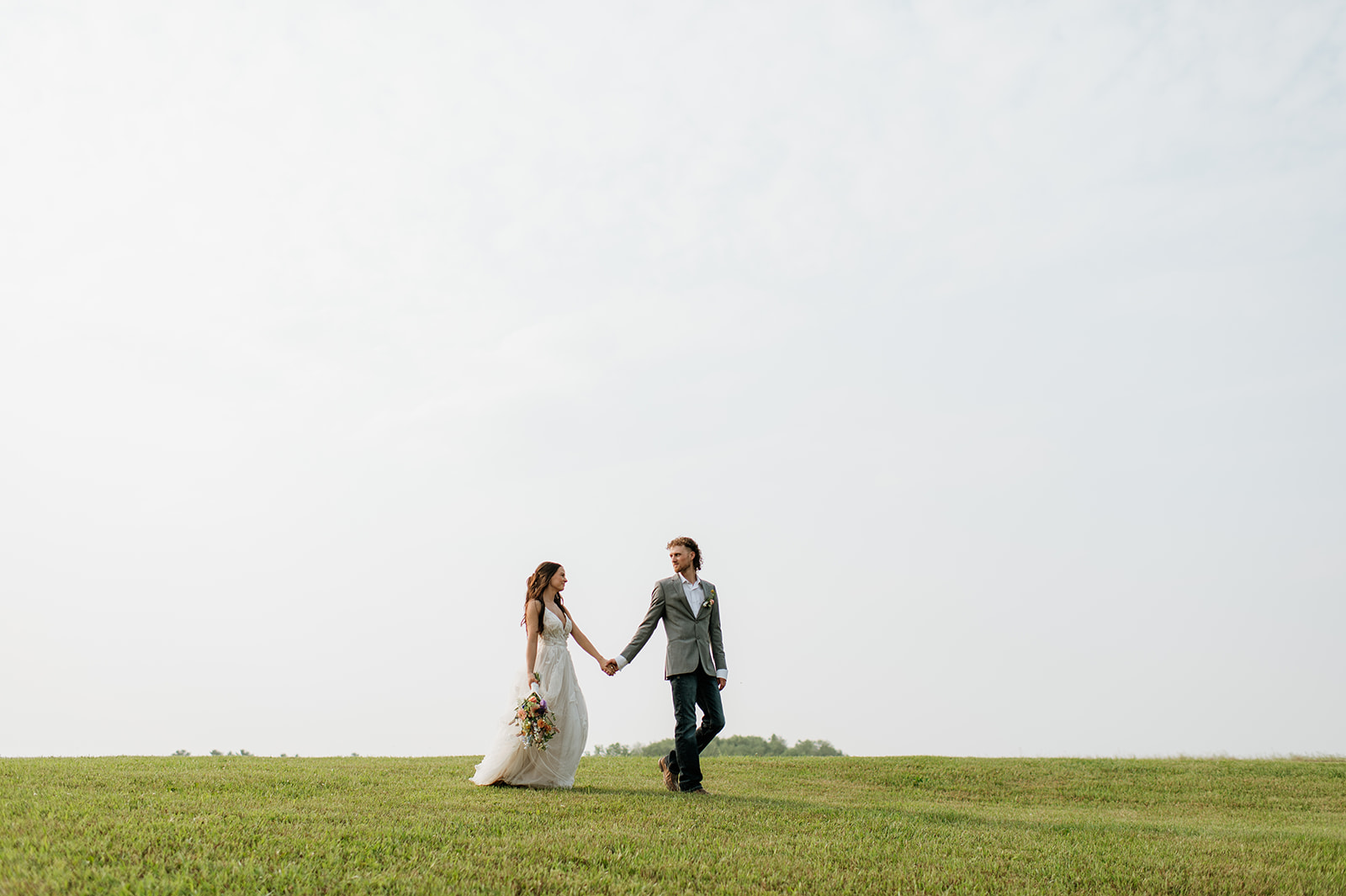 Bride and groom walking hand in hand in an open field at 5C Farms - Premier Indiana barn wedding venue in Albion