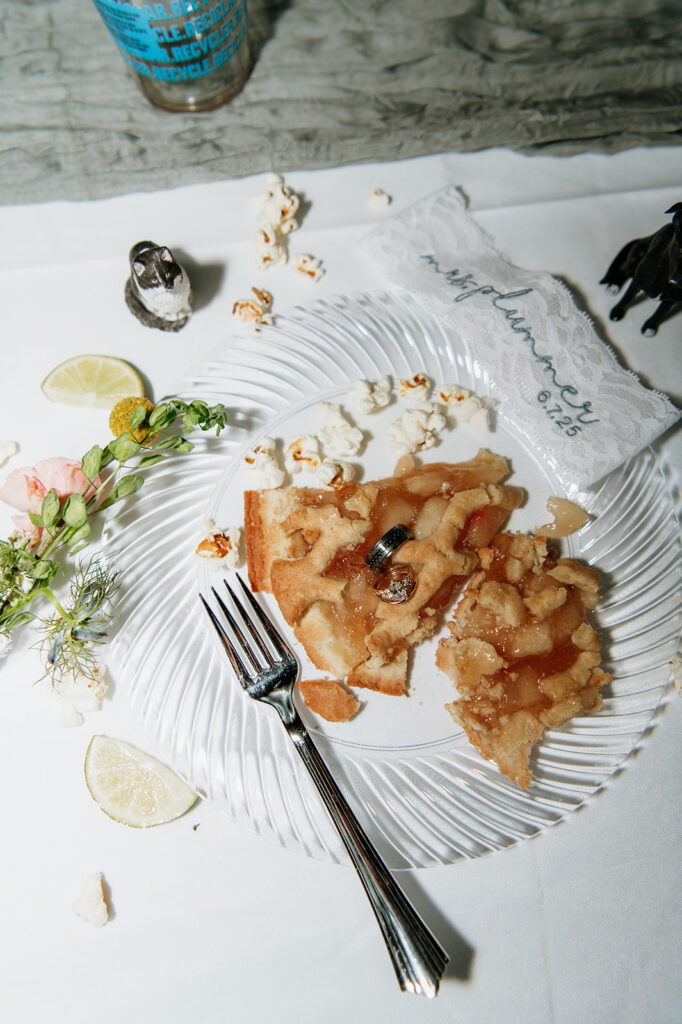 Close-up of dessert plate with a slice of pie, wedding rings placed on top, surrounded by popcorn, lime, and small figurines.