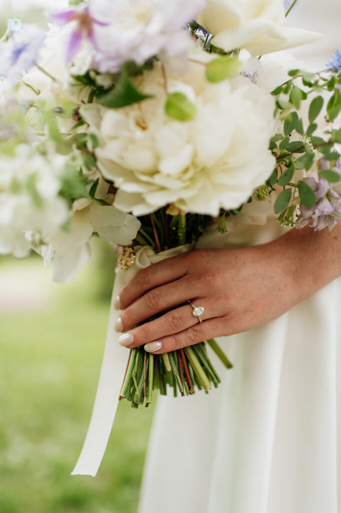 Close-up of bride holding her bouquet of ivory and purple flowers, showcasing her engagement ring.