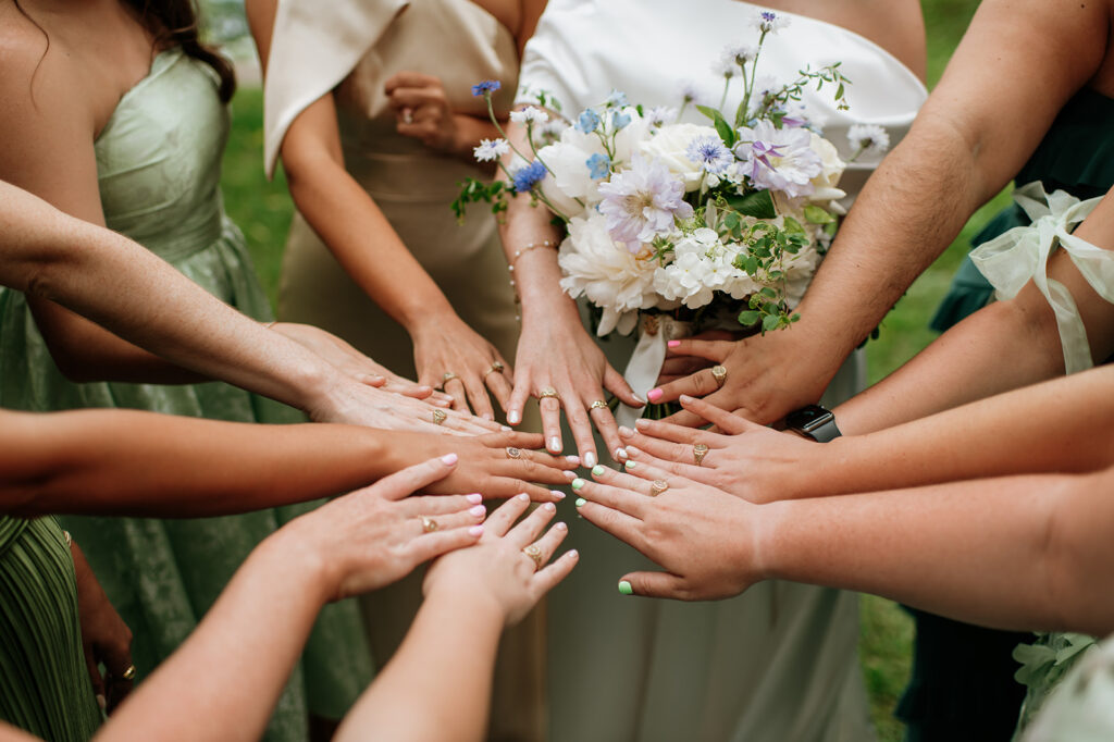 Close-up of bridesmaids and bride placing their hands together, showing matching rings and colorful nails.