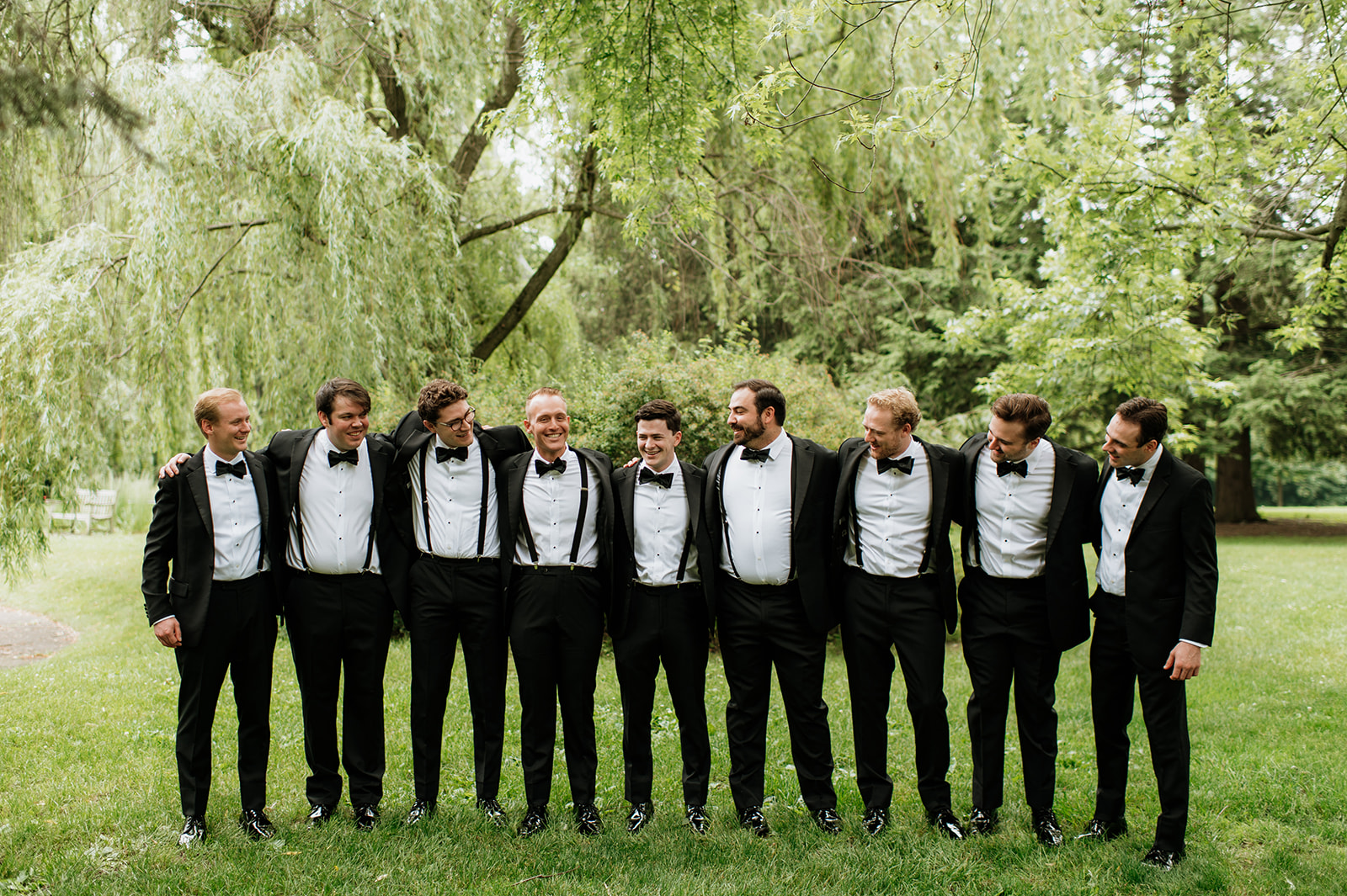 Groom with his groomsmen standing outdoors on Saint Mary’s College campus, arms linked and smiling.