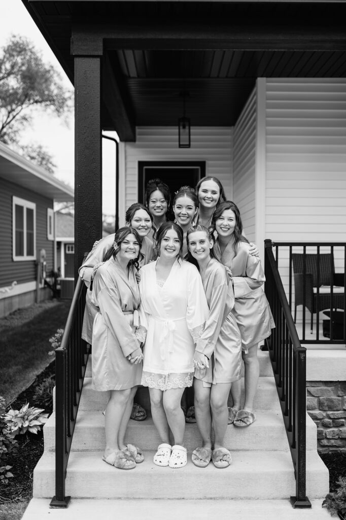 Black and white photo of the bride smiling on the porch, surrounded by her bridesmaids in matching robes.