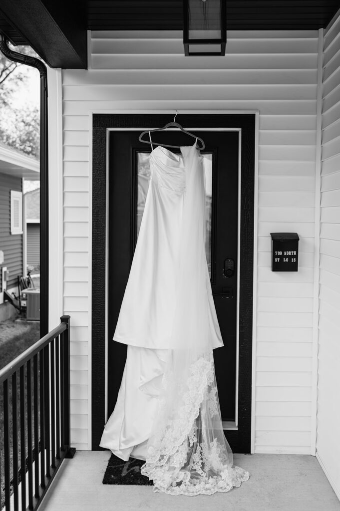 Bridal gown with lace train hanging on a front door outside the house.