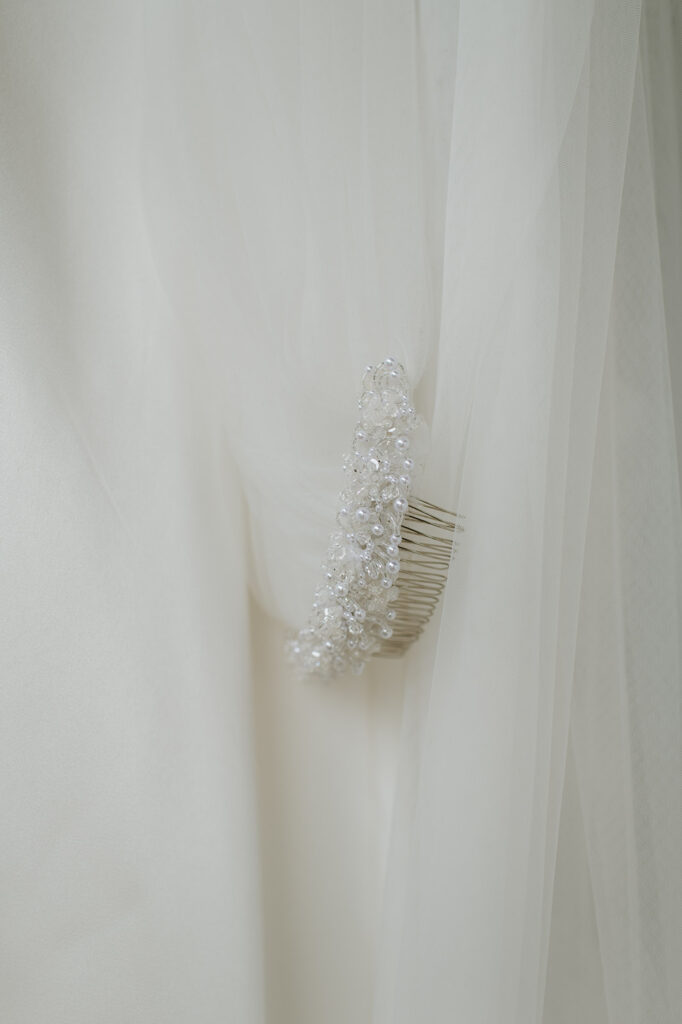 Close-up of brides veil comb, adorned with pearls and crystals, pinned into soft layers of tulle.