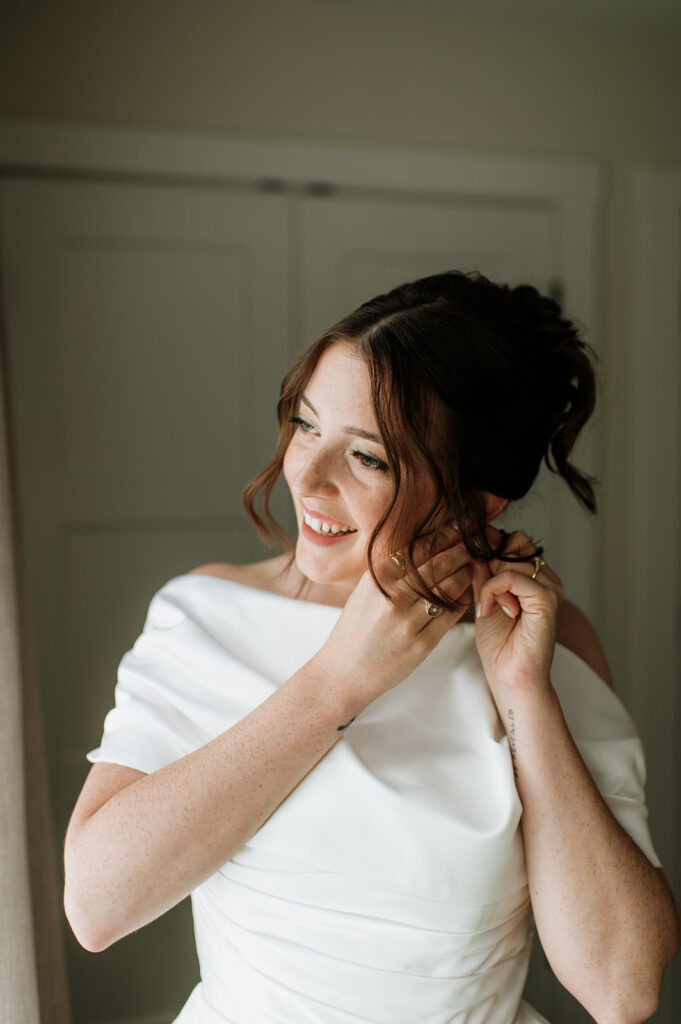 Bride smiling as she adjusts her earrings in natural light for her Notre Dame wedding