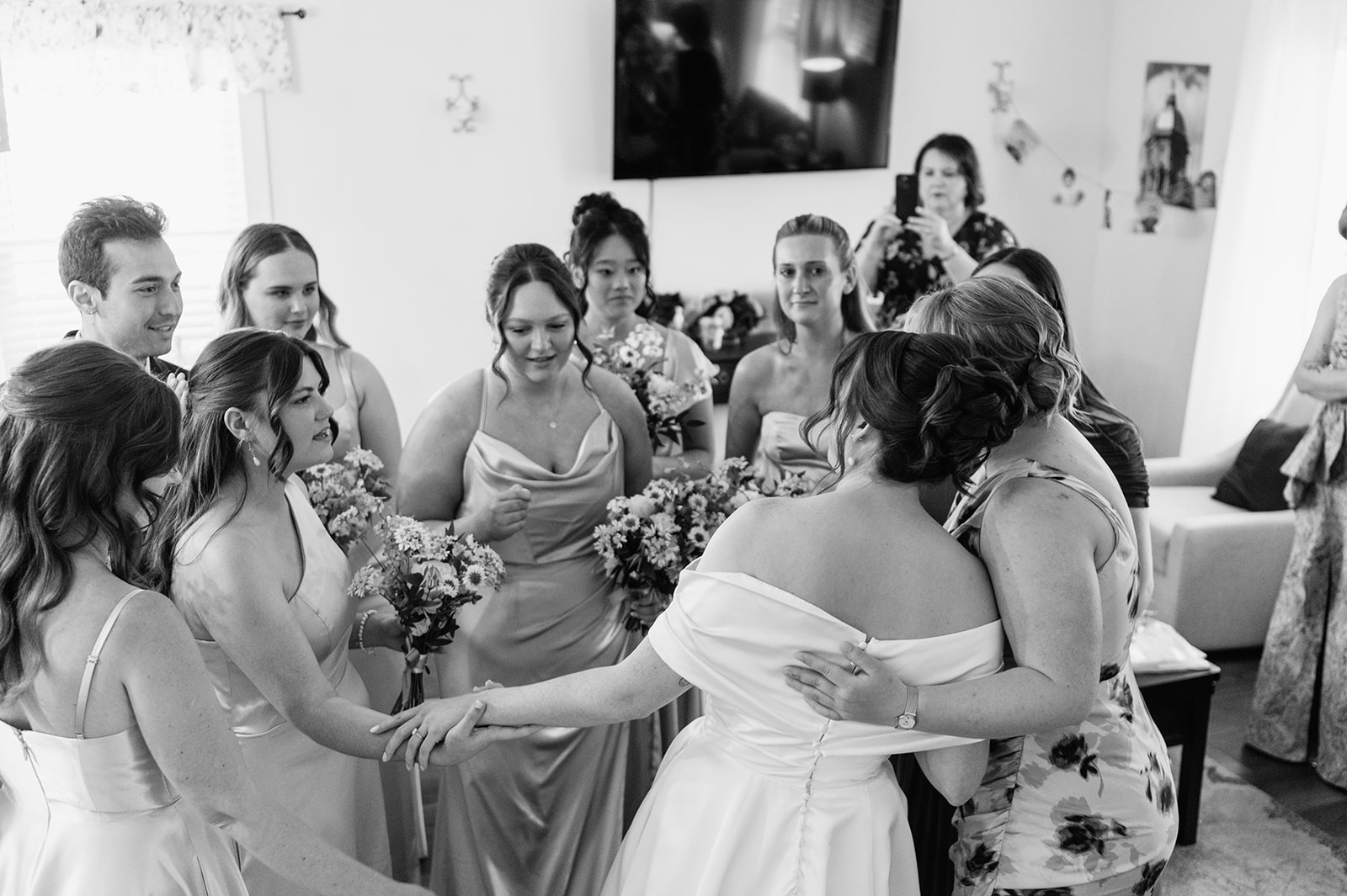 Candid black and white photo of a bride hugging friends after sharing a first look