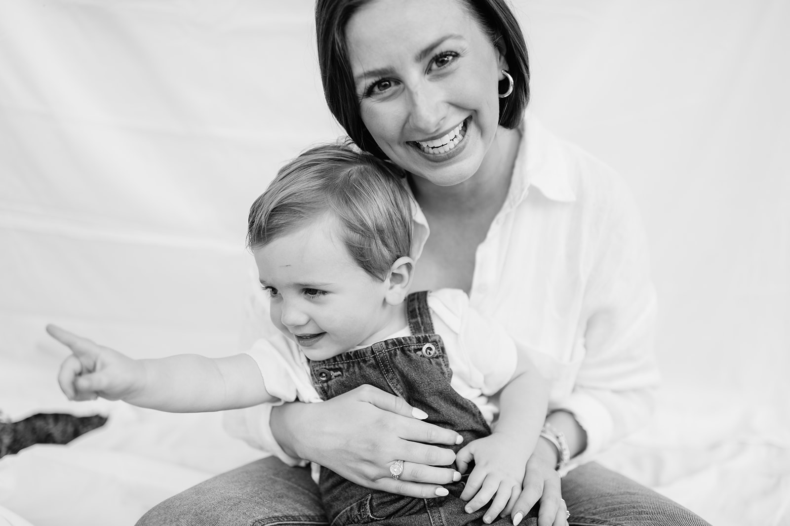 Mom laughing with her toddler on her lap in front of a white sheet backdrop.