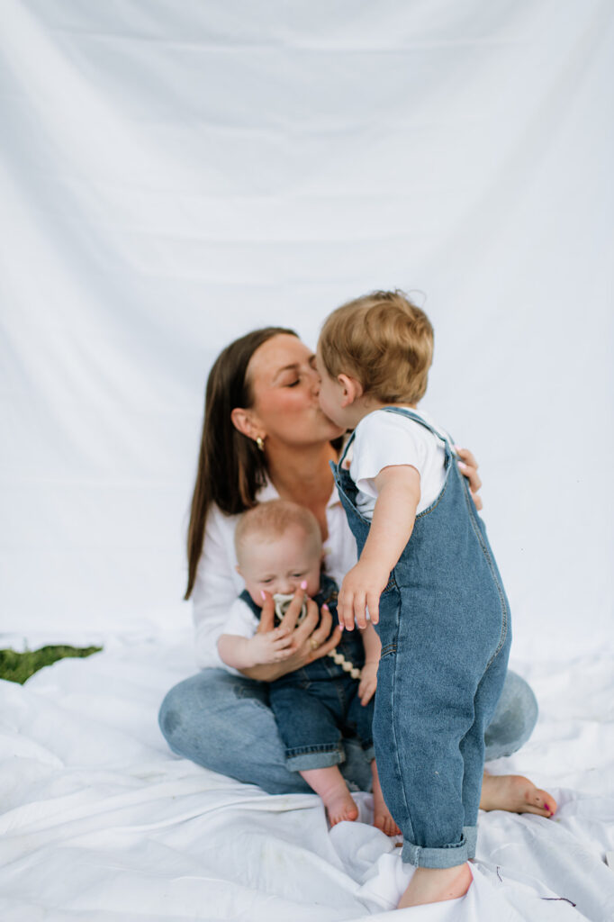 Toddler kissing mom while she holds the baby during their simple Chicago family photography session