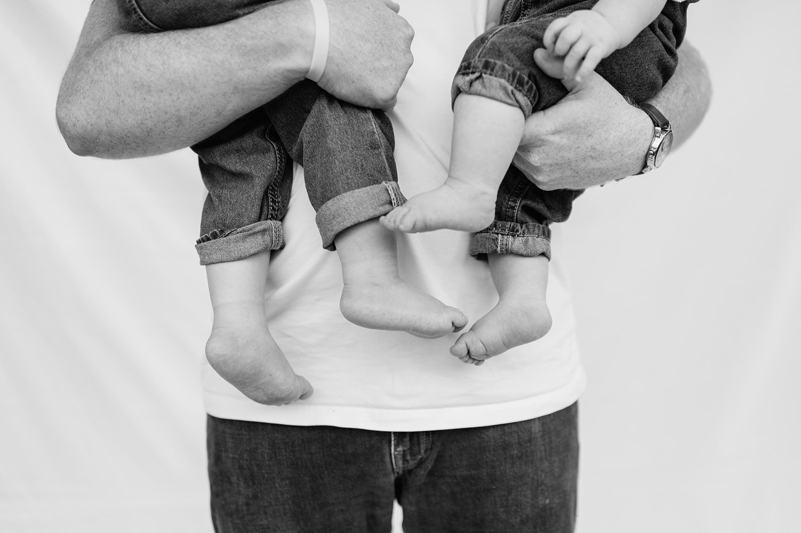 Black and white close up shot of a dad holding his two young shoes with their bare feet showing