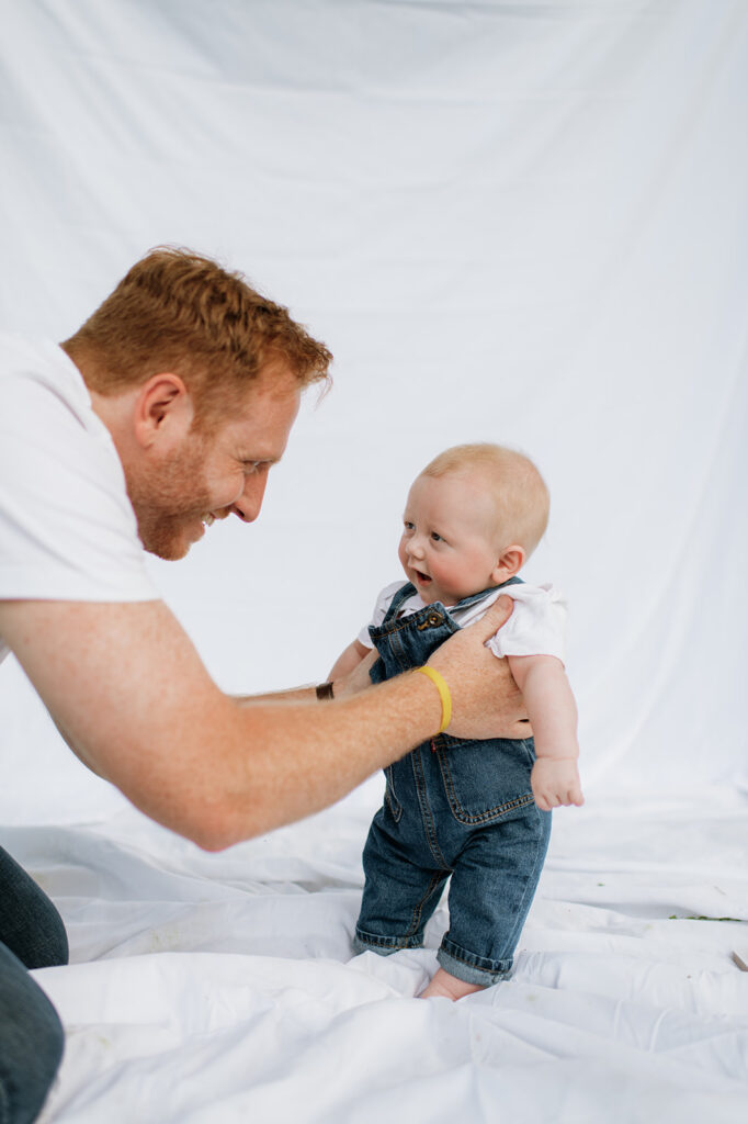 Dad crouching down to play with baby on the sheet backdrop.