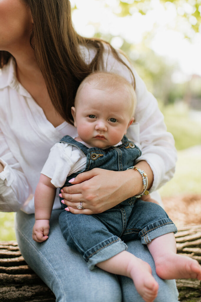 Close up of a baby boy sitting in his mothers lap and looking at the camera