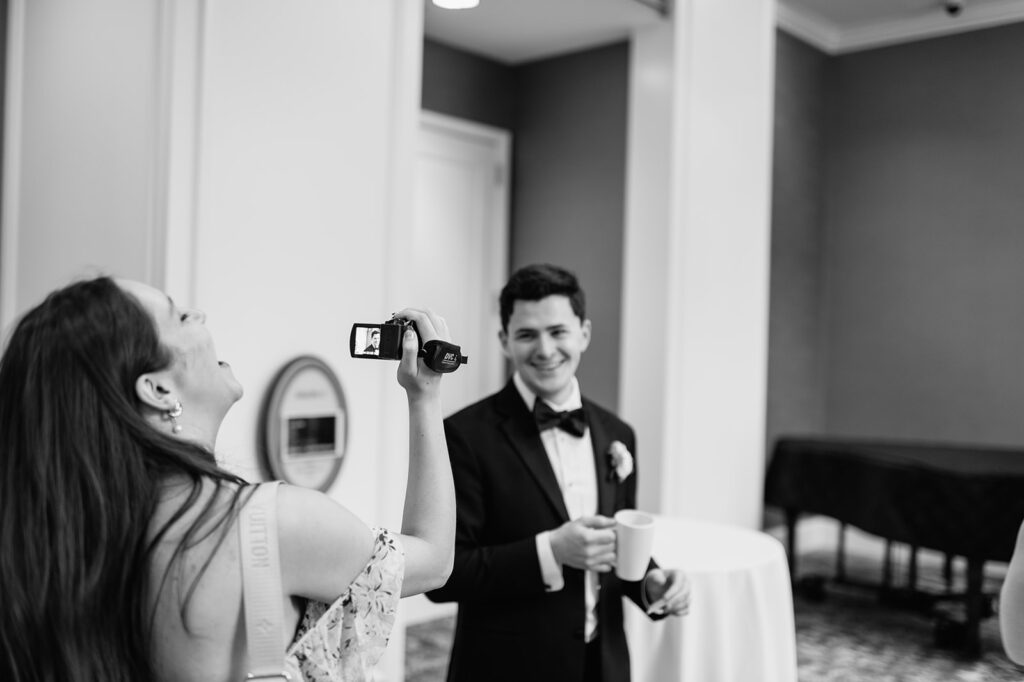 Black and white photo of a guest vide recording the groom during cocktail hour