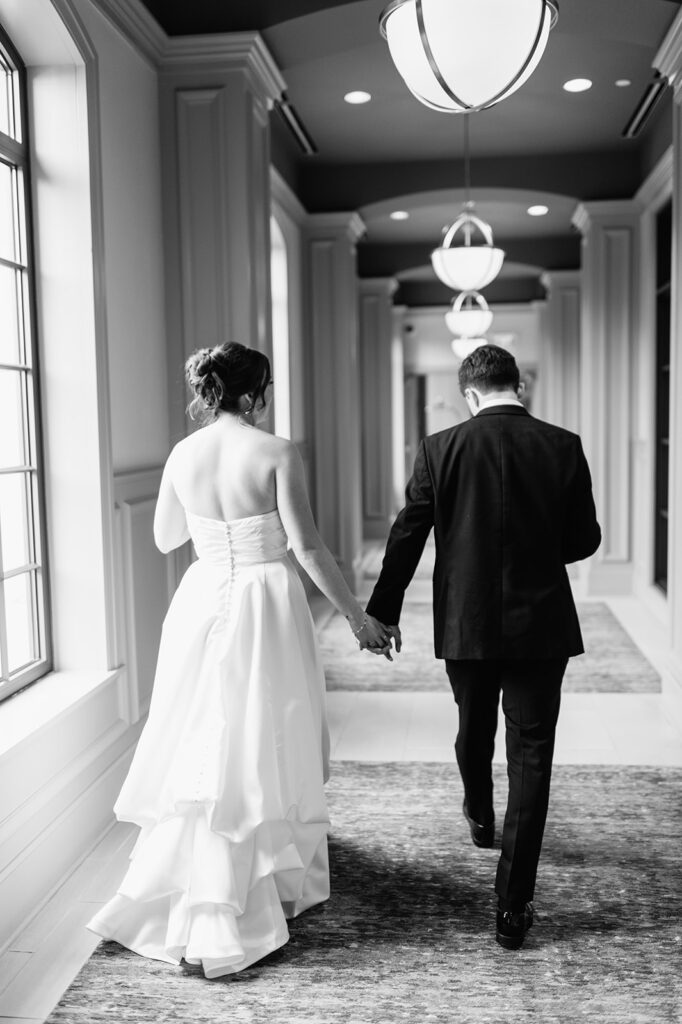 Black and white photo of a bride and groom walking down the hall together