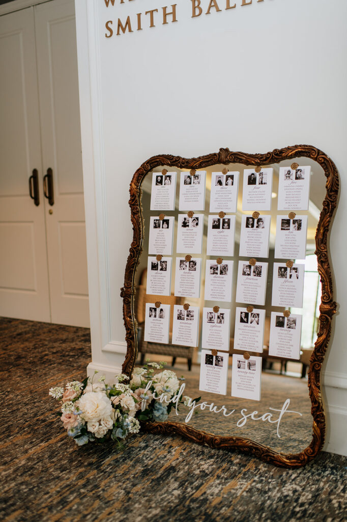 A vintage gold mirror holds the wedding seating chart with floral accents at the base in the Smith Ballroom at The Morris Inn.