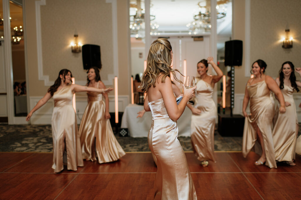Bridesmaids in champagne gowns laughing and dancing on the reception dance floor in the Smith Ballroom.