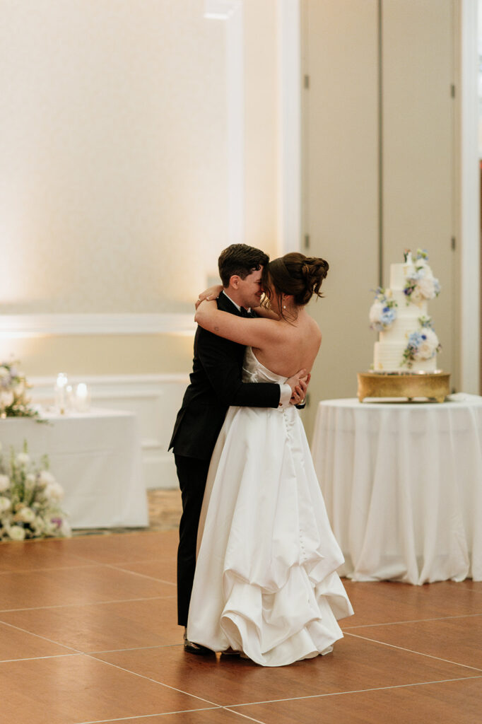 Bride and grooms romantic first dance in the Smith Ballroom with their wedding cake in the background.