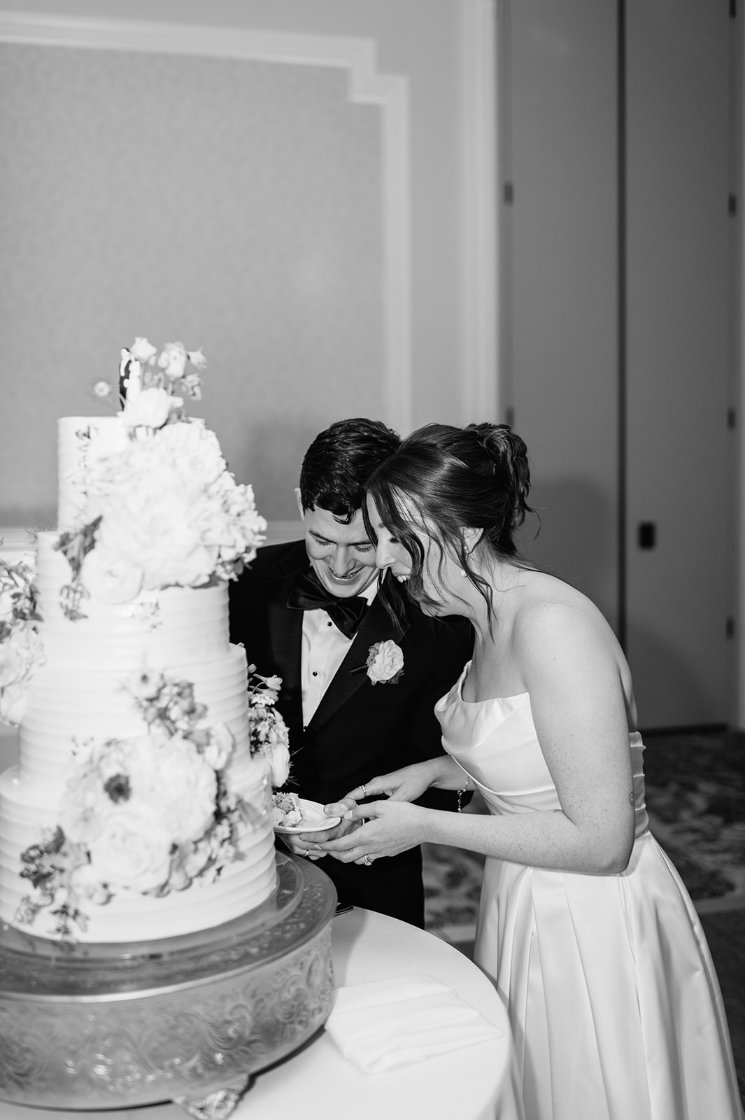 Black and white photo of a bride and groom cutting into their 4 tiered wedding cake